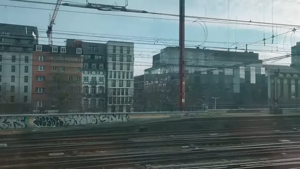 Trilhos de trem em primeiro plano e fachadas de prédios ao fundo vistas pela janela