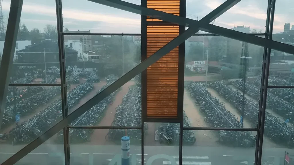 Fileiras de bicicletas estacionadas vistas através do vidro da estação com painéis laranja e vigas