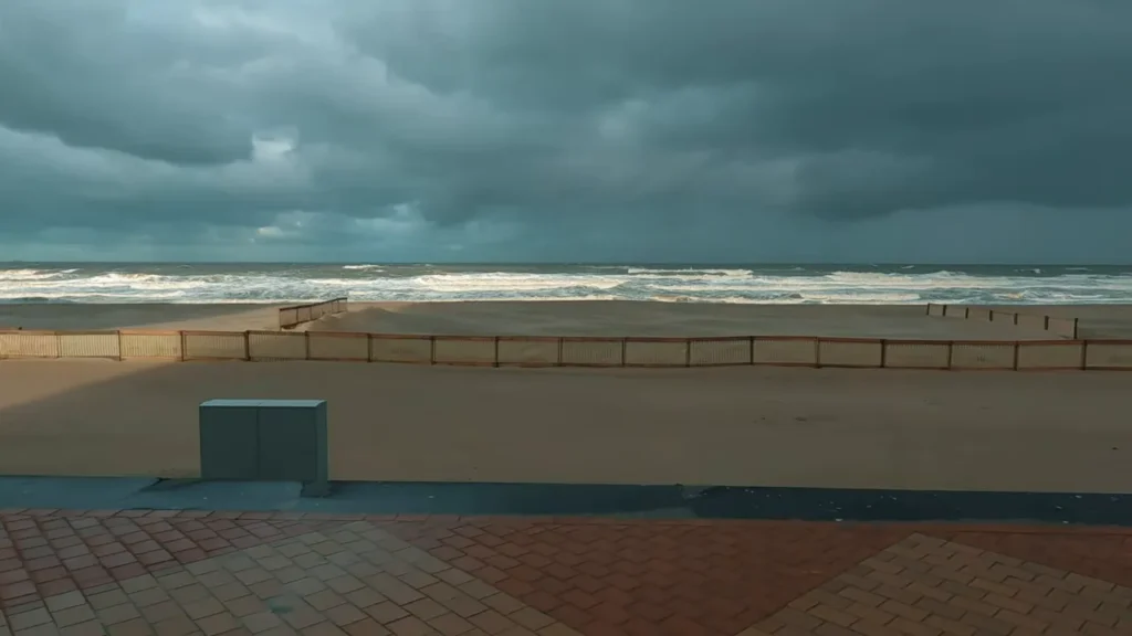 Praia de Blankenberge com cercas de proteção na areia e ondas do Mar do Norte sob céu carregado