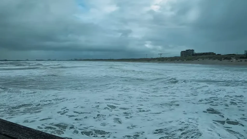 Vista do Mar do Norte e da orla de Blankenberge a partir do píer, mostrando ondas, faixa de areia e edifício na costa