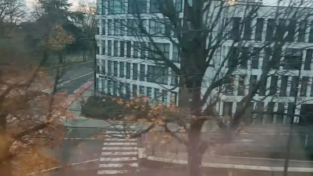 Vista através da janela do trem mostrando edifício, árvore e cruzamento urbano