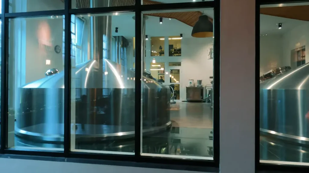Grandes tanques de brassagem de cervejaria em aço inox vistos através de janelas