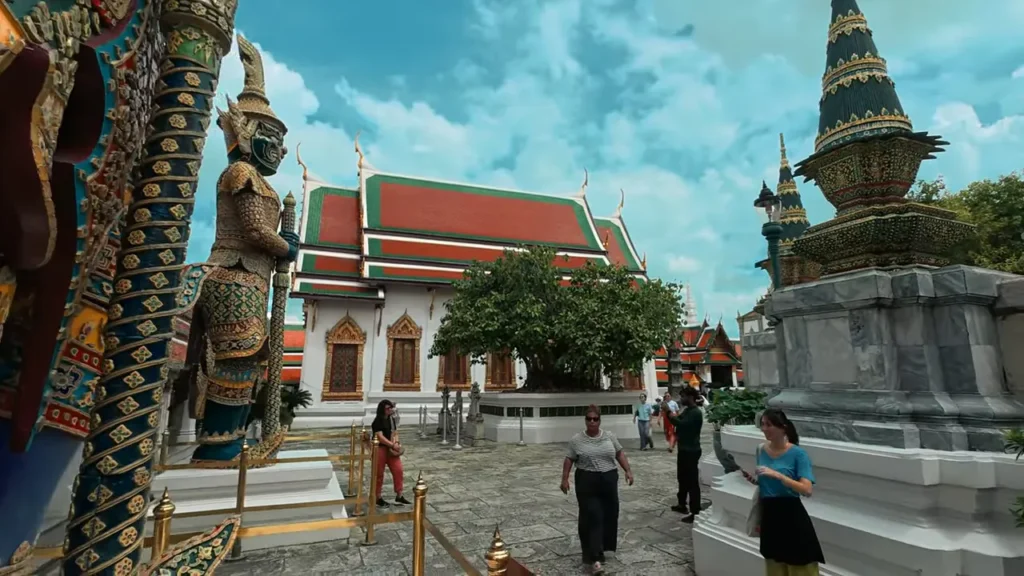 Pátio do Grand Palace em Bangkok com estátuas guardiãs, edifícios coloridos e turistas caminhando