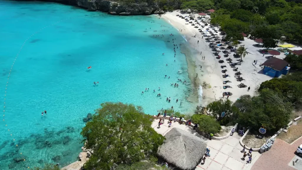 Foto aérea da enseada com areia branca, espreguiçadeiras e mar turquesa em Curaçao.