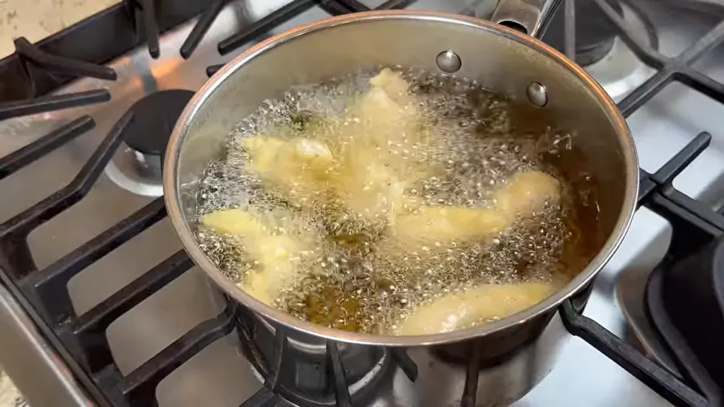 Frango empanado fritando com bolhas na panela, visto de cima