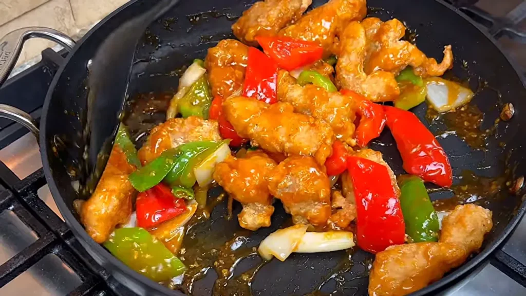 Frango agridoce pronto com frango empanado crocante, pimentões e cebola envoltos em molho agridoce brilhante